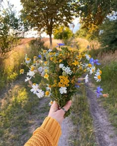 a person holding a bouquet of wildflowers in their hand on a dirt road