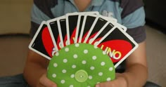 a young boy sitting on the floor holding four playing cards and a green object in his hands