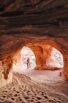 two people are standing in the middle of a large rock formation with sand and water