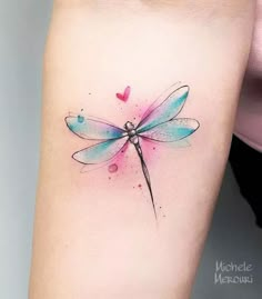 a watercolor dragonfly tattoo on the right arm and shoulder, with hearts in the background