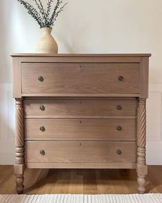 a wooden dresser sitting on top of a hard wood floor next to a white vase