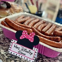 some hot dogs in pink paper containers with minnie mouse stickers on them and a sign that says, her disney does