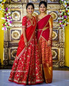 two women standing next to each other wearing red and gold outfits with flowers in the background