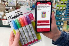 a person holding up a cell phone in front of a display of sharpie pens