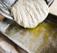 a metal bowl filled with white dough on top of a wooden table next to a spoon