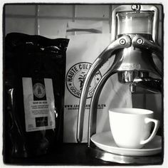 black and white photograph of coffee being poured into a cup next to a bag of coffee