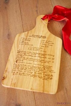 a wooden cutting board with a red ribbon around it on a wood floor next to a bottle of wine