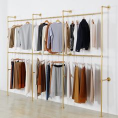 a rack with clothes hanging on it in front of a white wall and wooden floor