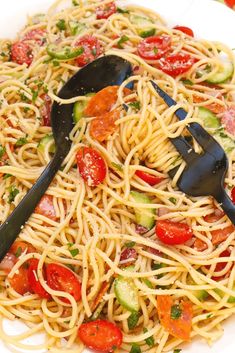 a white plate topped with pasta and veggies next to a black serving spoon