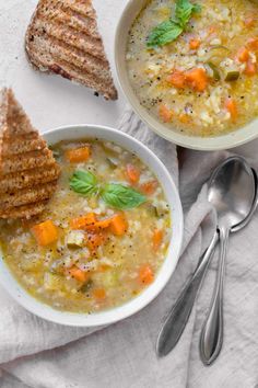 two bowls filled with soup next to toasted bread on a white cloth and spoons