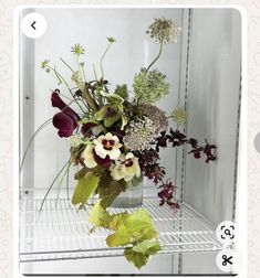 a vase filled with lots of flowers on top of a metal shelf next to a mirror