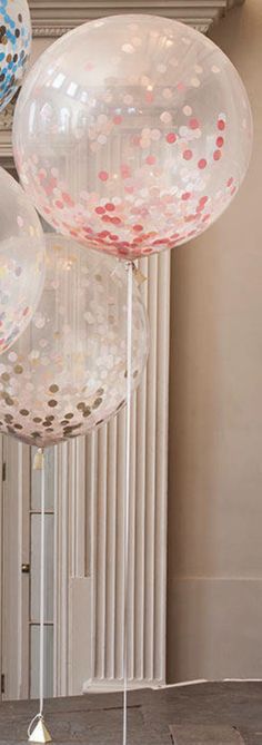 three clear balloons with confetti on them in front of a white wall and floor