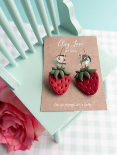 a pair of strawberry shaped earrings sitting on top of a table next to a pink flower