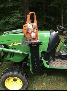 a green tractor parked in the grass next to trees