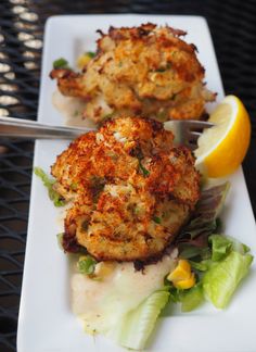 two crab cakes on a white plate with lemon wedges and lettuce next to them