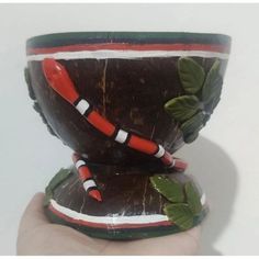 a hand is holding a small cup that has leaves on the rim and red, white, and green trim