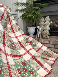 a living room with a fireplace and christmas decorations on the mantel, as well as a large plaid quilt