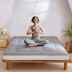 a woman is sitting in the middle of a yoga pose on a mattress with her hands together