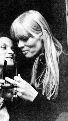 black and white photograph of two women looking at something in her hand while the woman is brushing her teeth