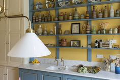 a kitchen with blue cabinets and yellow walls is pictured in this image, there are many vases on the shelves above the sink