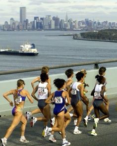 a group of women running across a bridge over looking the water and a city skyline