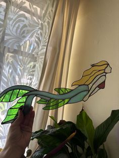 a person is holding up a stained glass dragon on a window sill next to a potted plant