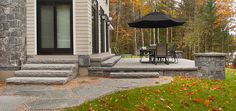 an outdoor patio with steps, table and umbrella in front of a stone house on a fall day