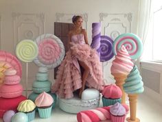 a woman in a pink dress sitting on top of a table surrounded by candy and lollipops