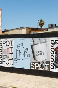 a wall with posters on it in front of a building and palm trees behind it