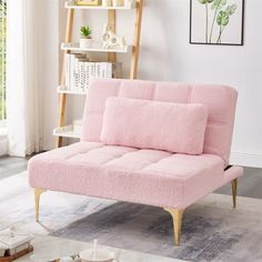 a pink couch sitting on top of a wooden floor next to a book shelf and window