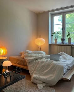 an unmade bed sitting next to a window in a room with two lamps on either side