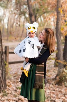 a woman holding a child wearing an owl costume in front of some trees and leaves