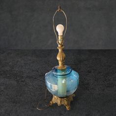 a blue glass table lamp with a gold base and light bulb on top, sitting on a black surface