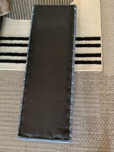 a piece of black leather sitting on top of a white and black striped carpeted floor