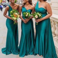 three bridesmaids in green dresses posing for a photo on the street with their bouquets