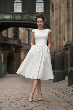 a woman in a white dress is standing on a brick road and posing for the camera