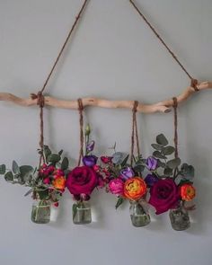 three mason jars filled with flowers hanging from a branch