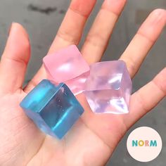 three different colored glass cubes held in someone's hand with the word norm on it