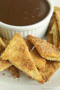 some fried food on a white plate with dipping sauce in the bowl and bread sticks