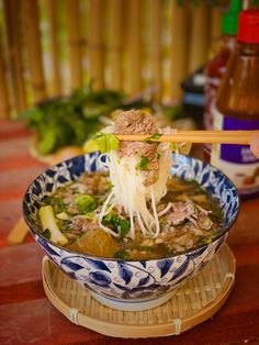 a person holding chopsticks above a bowl of soup