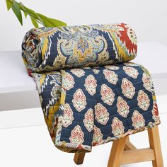 a blue and red blanket sitting on top of a wooden stool next to a plant