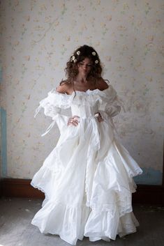 a woman in a white dress is standing against a wall with flowers on her head