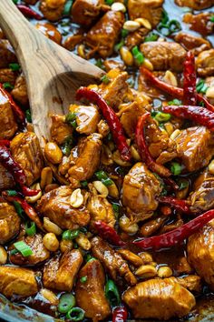 chicken and cashews are being cooked in a skillet with a wooden spoon