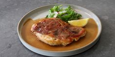 a white plate topped with meat covered in gravy next to a green salad