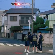 three people standing at an intersection waiting for the light to turn on their way home