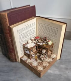 an open book with miniature food items on top and in the middle, sitting on a table