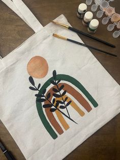 a tote bag sitting on top of a wooden table next to paints and brushes