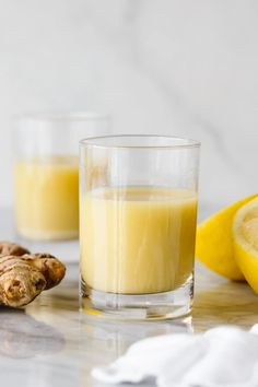 two glasses filled with orange juice next to a lemon and ginger on a marble table