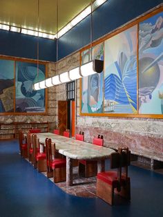 a long table with red chairs is in the middle of a room that has paintings on the walls