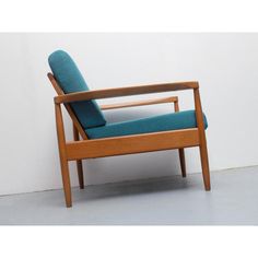 a wooden chair with a blue cushion on the back and arm rests against a white wall